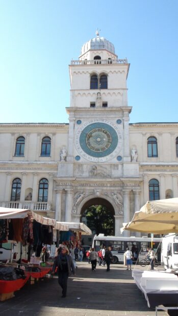 The historic clock tower stands tall in the Trieste city center with people walking nearby, 4K Mobile Wallpaper