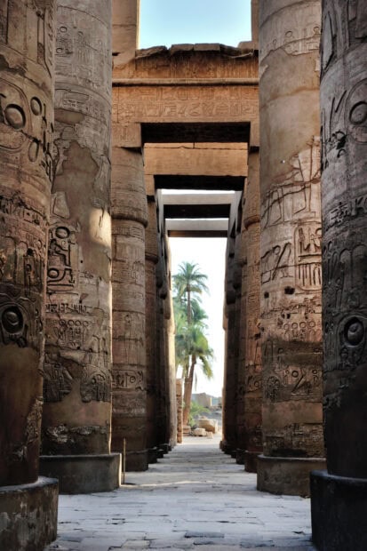 Ancient Egyptian columns with hieroglyphics and palm trees visible through the passageway