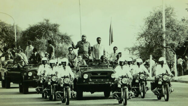 A historic parade with a military leader and escorts riding motorcycles on the street