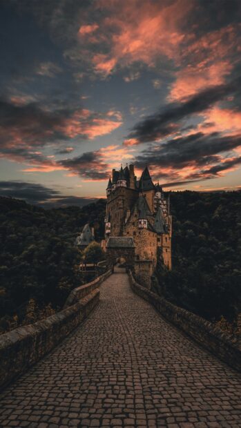 A historic castle on a cobblestone path under a dramatic sunset sky