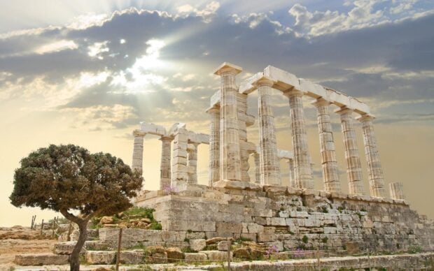 Ancient ruins of a temple under a cloudy sky with sunlight rays visible