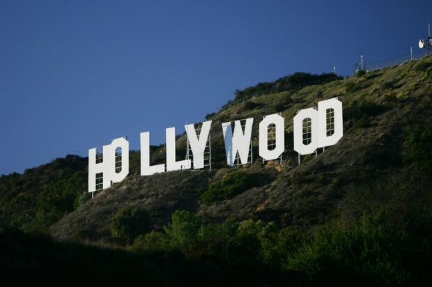 The iconic Hollywood sign stands prominently on the hillside under a clear blue sky
