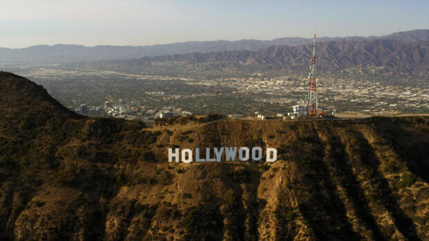 A panoramic view of the Hollywood sign on a hillside with cityscape and mountains in the background