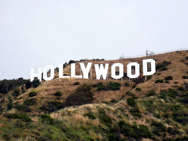 The famous Hollywood Sign stands prominently on a hillside surrounded by dry grass and greenery
