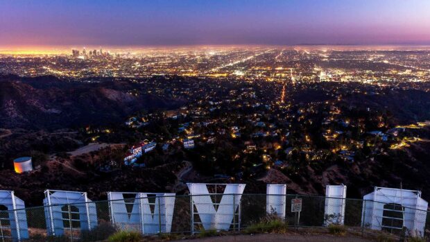 View of the Hollywood Sign from behind overlooking the cityscape at night with city lights on the hills