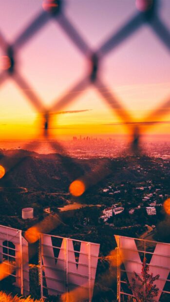 View of the Hollywood sign and Los Angeles cityscape at sunset behind a fence with hills in the background