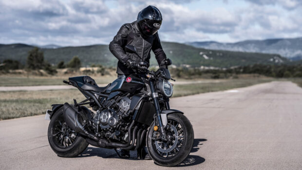 A rider on a Honda CB1000R wearing black gear stands on a countryside road, 4K Desktop Wallpaper
