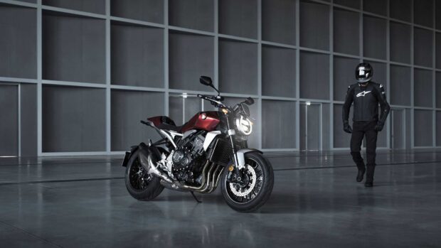 A Honda Cb1000R motorcycle is parked inside a spacious modern garage with a rider in black gear nearby, HD Desktop Wallpaper