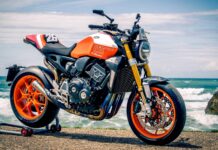 High-performance Honda racing motorcycle with orange and black accents, displayed on a seaside backdrop, featuring advanced suspension and aerodynamic design.