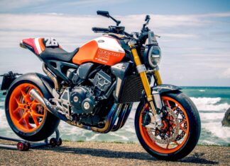 High-performance Honda racing motorcycle with orange and black accents, displayed on a seaside backdrop, featuring advanced suspension and aerodynamic design.
