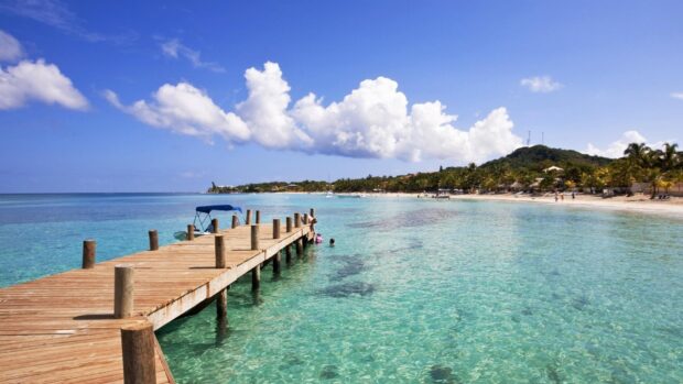 Clear turquoise water with a wooden pier on the Honduras coast under a blue sky