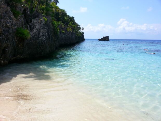 Clear water and rocky coast of Honduras beach with swimmers in the sea