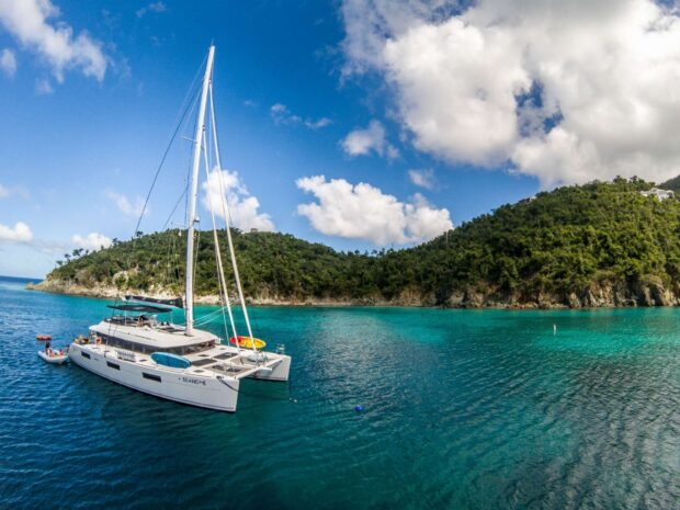 A sailboat near a green lush island in Honduras with clear blue water and sky