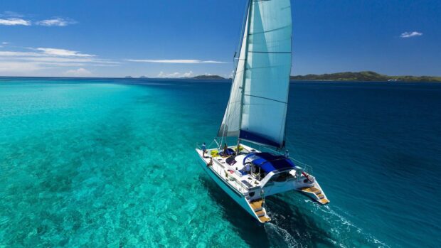 A sailboat sailing on clear turquoise waters in Honduras with distant islands visible