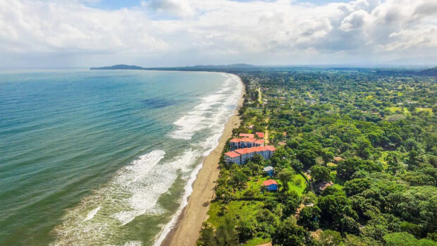 Aerial view of Honduras coastline with lush greenery and red roofed buildings along the beach