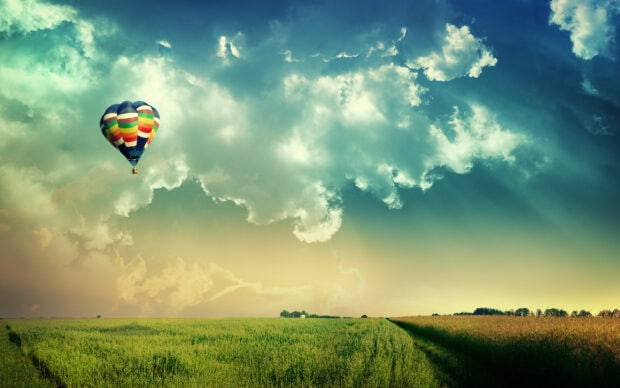 A colorful hot air balloon floating over a vast green field under a cloudy sky