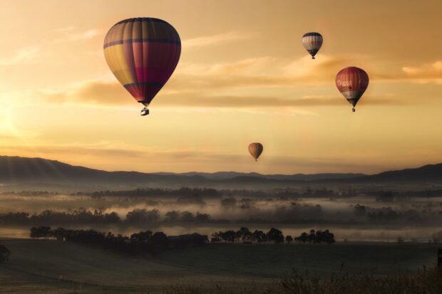 A scenic view of multiple hot air balloons floating over misty hills at sunrise