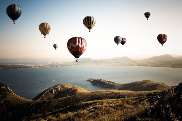 Colorful hot air balloon flying over the sea and mountainous landscape at sunset
