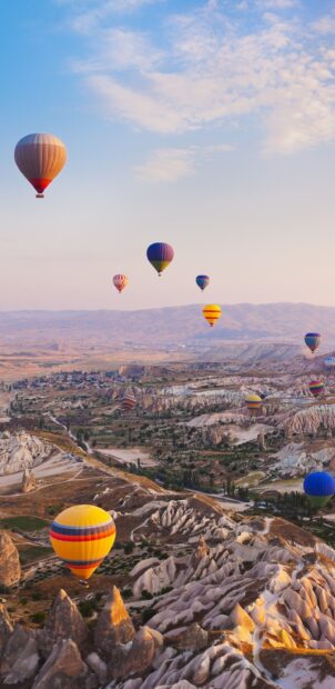 Colorful hot air balloon flying over rocky terrain during sunrise in Cappadocia valley