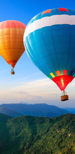 Two colorful hot air balloons floating over green mountains during clear blue sky