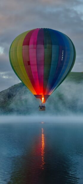 Colorful hot air balloon floating over misty water at sunrise
