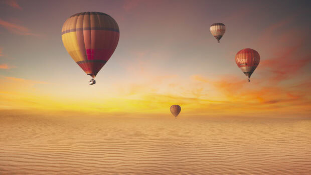 Colorful hot air balloon flying over desert dunes at sunset sky
