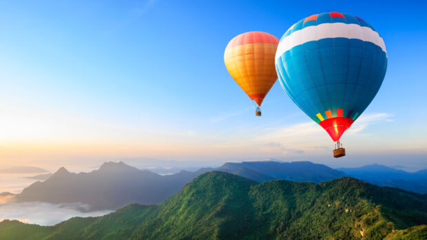 Two colorful hot air balloon floating over green mountains during sunrise