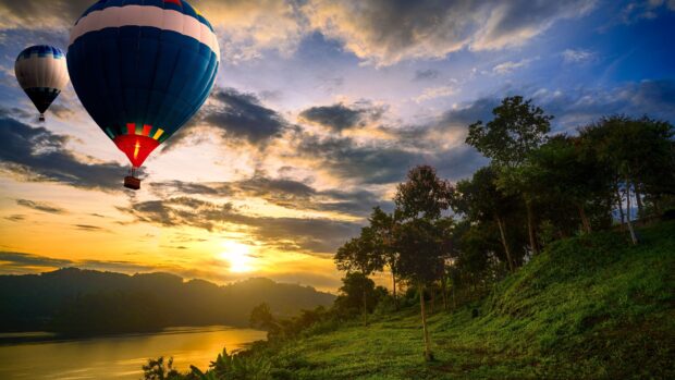 Two colorful hot air balloons floating over a green hillside at sunset