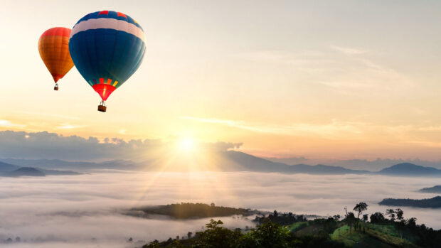 Two colorful hot air balloons flying over misty mountains at sunrise with clear sky