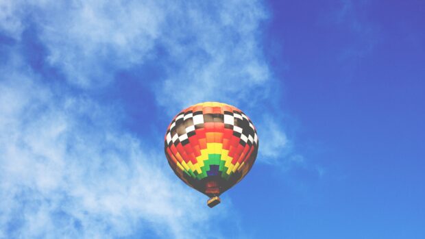 A colorful hot air balloon floating high in a bright blue sky with scattered clouds