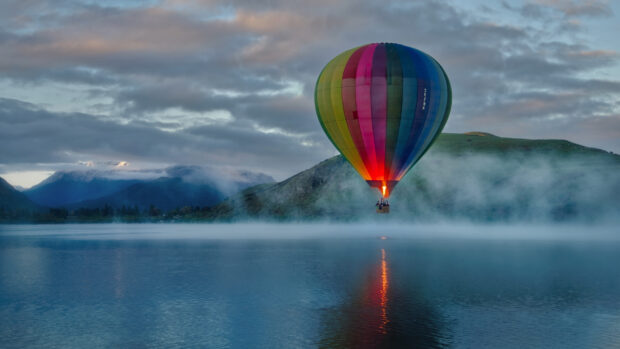 A colorful hot air balloon floating over a misty lake with mountains in the background
