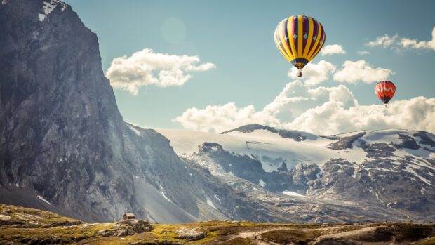 Colorful hot air balloon floating over rocky mountains and snowy peaks in clear sky