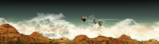 Colorful hot air balloon flying over a desert landscape under cloudy sky