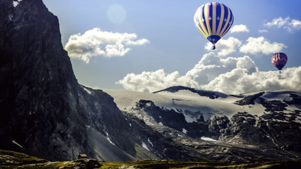 Colorful hot air balloon flying over rocky mountain landscape with snow caps