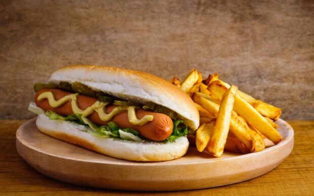 A hot dog with mustard pickles and lettuce served with crispy fries on a wooden plate