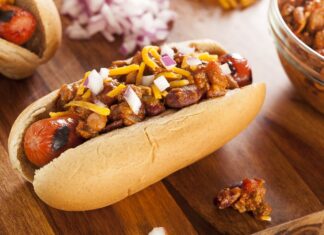 A chili topped hot dog with chopped onions and shredded cheese on a wooden surface