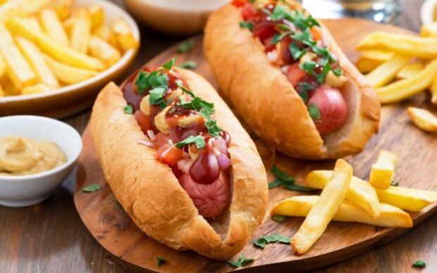 Hot dog with mustard ketchup and herbs served with French fries on a wooden plate
