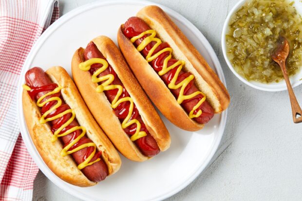 Three hot dogs with ketchup and mustard on a plate with relish on the side