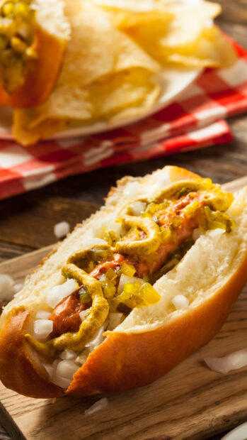 A hot dog with mustard onions and relish served in a bun on a wooden board