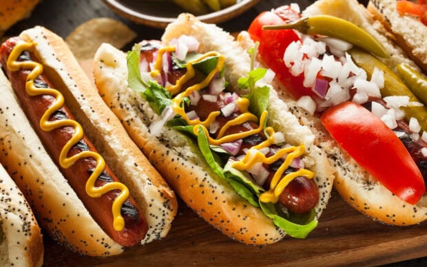 A close up of hot dog with mustard and fresh vegetables on a poppy seed bun