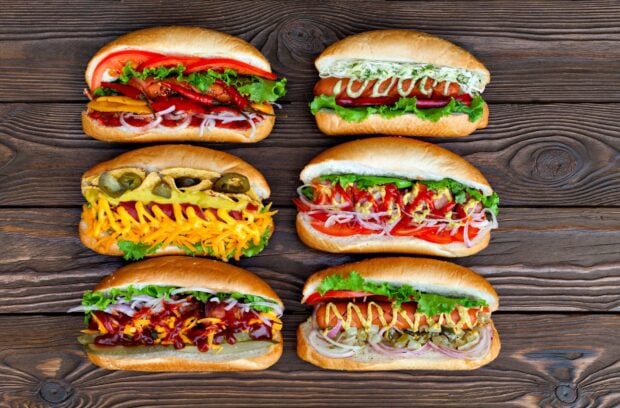 Six hot dog sandwiches with various toppings on a wooden surface showcasing different hot dog styles