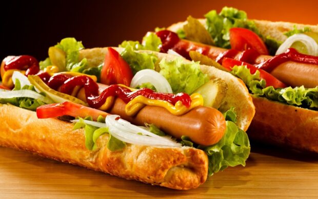 A delicious hot dog topped with ketchup mustard lettuce onions and tomato slices in a fresh bun