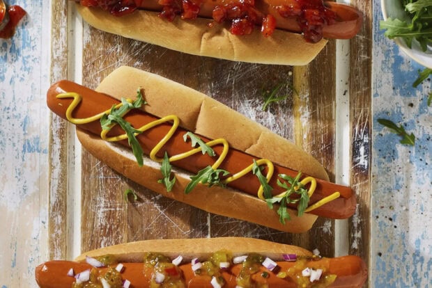 A fresh hot dog with mustard and greens on a wooden surface