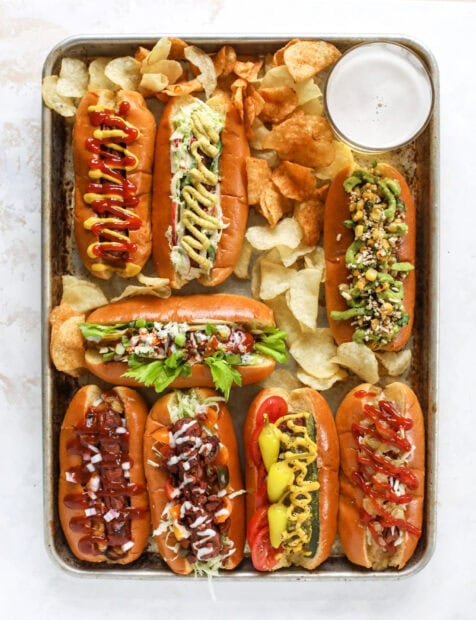 A variety of hot dog with different toppings arranged on a tray surrounded by potato chips
