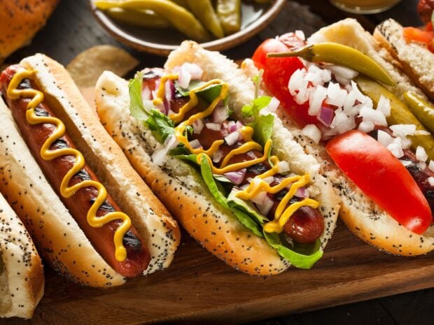 A close up of grilled hot dog with mustard and fresh lettuce on a poppy seed bun