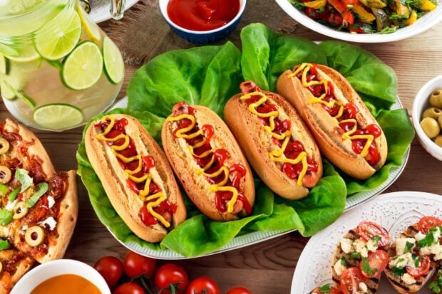 Four hot dog sandwiches served with ketchup and mustard on fresh lettuce leaves