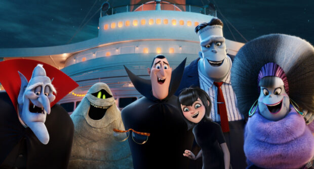 The main characters from Hotel Transylvania stand together on a ship deck smiling and posing for a group photo