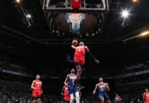 A Houston Rockets player soaring for a dunk during a basketball game against the Nets in a crowded arena