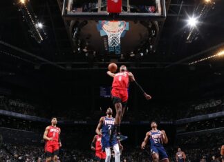 A Houston Rockets player soaring for a dunk during a basketball game against the Nets in a crowded arena