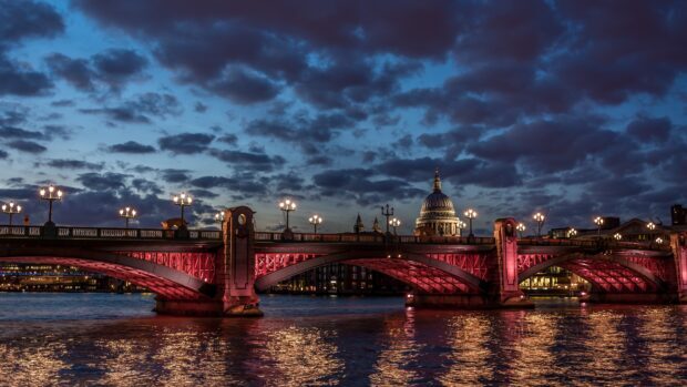 The River Thames showcases a lit bridge with a historic dome under a cloudy evening sky, 4K Desktop Wallpaper